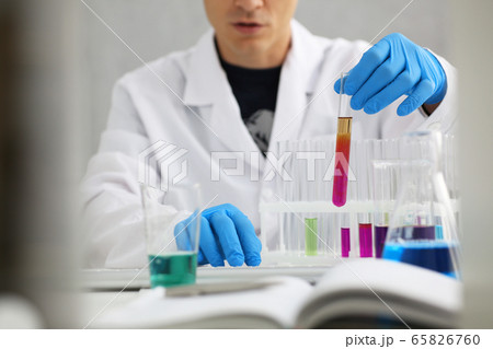 A male chemist holds test tube of glass in his hand overflows a liquid solution A male chemist holds test tube of glass in his hand overflows a liquid solution 65826760