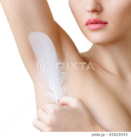 Woman holds white feather near clean armpit. Depilation concept. 65829343