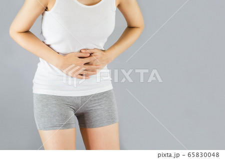 young woman in white undershirt and gray shorts , grabbing belly, She have a stomachache . Health Care Concept. 65830048