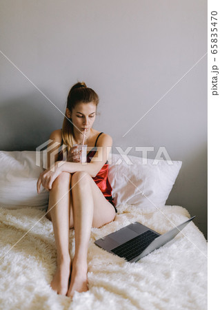 Young woman sipping milkshake and watching movie on bed Young woman sipping milkshake and watching movie on bed 65835470