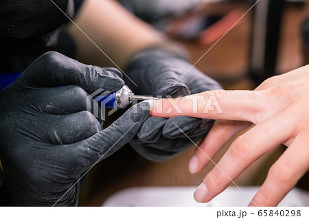 Manicurist use electric nail file drill in beauty salon. Perfect nails manicure process close up with burst flying debris. 65840298