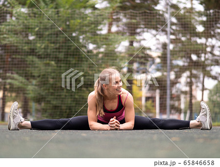 Muscular blond smiling attractive girl doing middle split stretching on the sports area outdoor in summer, selective focus. 65846658