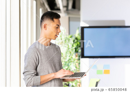 横向きに立ったままでノートパソコンをいじっている様子 の写真素材