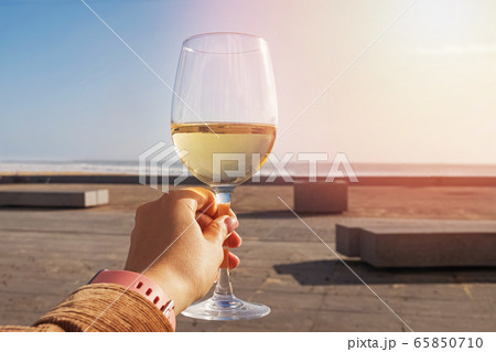 Woman's hand holding a glass of white wine on the open terrace of a street restaurant 65850710