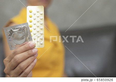Woman hand holding contraceptive pills and condom sitting on sofa background. Woman hand holding contraceptive pills and condom sitting on sofa background. 65850926