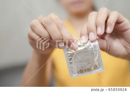Woman hand holding condom sitting on sofa 65850928