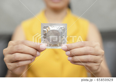 Woman hand holding condom sitting on sofa 65850929