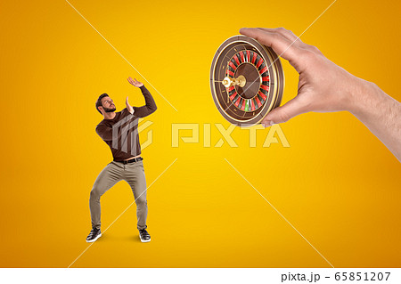 Man in casual clothes protecting himself from hand with a roulette on yellow background 65851207