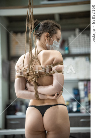 Shibari class - topless woman in medical mask with tied hands behind her back 65852160