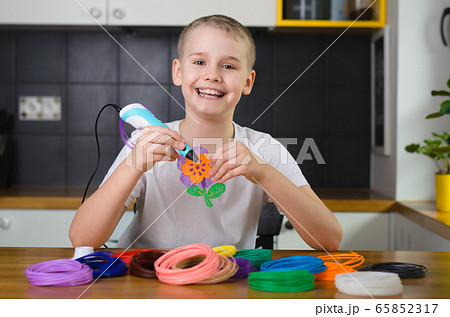 Child using 3D pen. Happy boy making flower from colored ABS plastic. 65852317