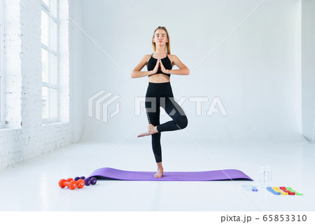 Girl practicing yoga, standing in vrksasana exercise with namaste, tree pose. Female meditation at white loft studio background. 65853310
