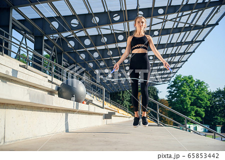 fitness and lifestyle concept - woman doing sports outdoors. girl with skipping rope. 65853442