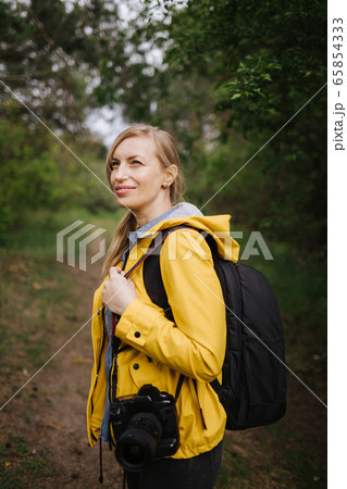 Charming woman standing at forest with backpack and camera Charming woman standing at forest with backpack and camera 65854333