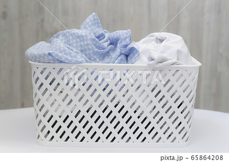 Blue and white dirty things in a white plastic laundry basket on a gray wall background. Washing, home cleaning 65864208
