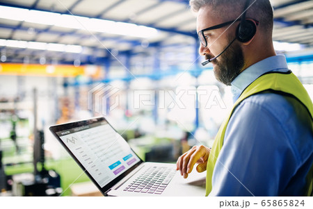 Side view of technician or engineer with headset and laptop standing in industrial factory. 65865824