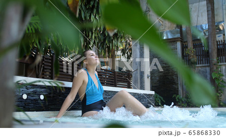 Beautiful young woman relaxes in a hydromassage jacuzzi, in swimming pool. Concept: spa procedures, body massages, spa cream, relax, spa water treatments Beautiful young woman relaxes in a hydromassage jacuzzi, in swimming pool. Concept: spa procedures, body massages, spa cream, relax, spa water treatments 65868330