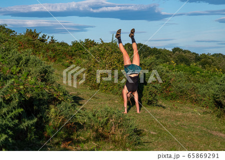 Young girl in a hat doing a handstand on the green hill. 65869291