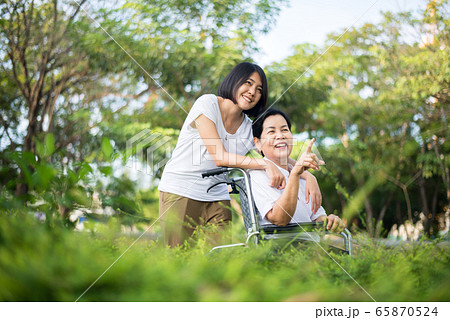 Senior care insurance concept,Caregiver take care to elderly asian woman sitting on wheelchair at nature 65870524