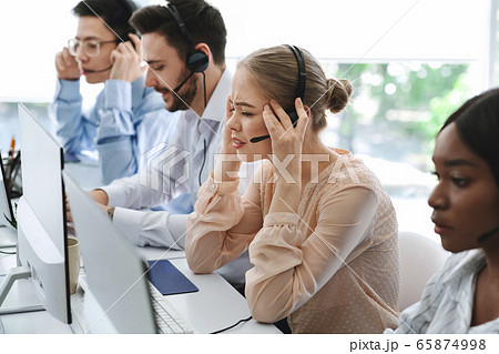 Busy call centre assistants with headsets working in front of computer monitors in open space office Busy call centre assistants with headsets working in front of computer monitors in open space office 65874998