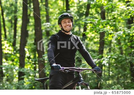 Cheerful cyclist posing with bike over forest background 65875000