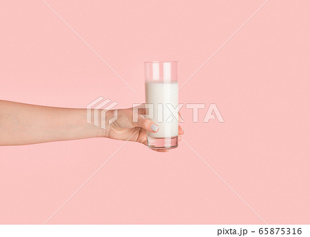 Girl hand showing glass full of milk on pink background, closeup 65875316