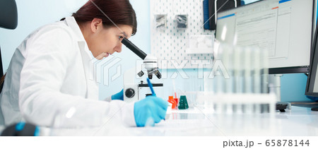 Side view of brunette lab technician looks at microscope in laboratory. 65878144