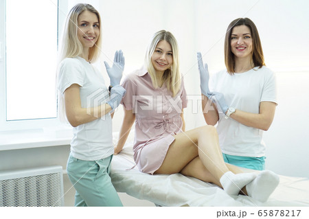 Two beauticians or doctors put a glove and smile. The patient lies on couch 65878217