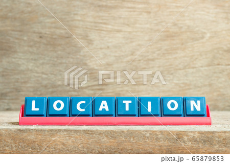 Tile letter on red rack in word location on wood background 65879853