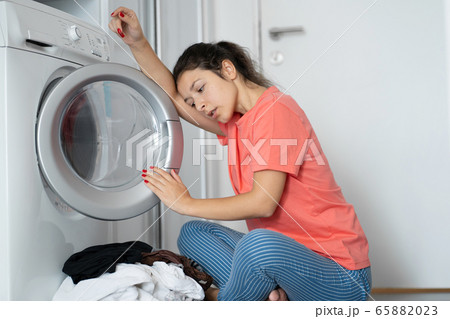 A girl loads dirty laundry into a washing machine A girl loads dirty laundry into a washing machine 65882023