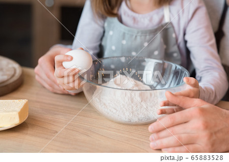 Little girl cracking egg to bowl, helping father with cooking pastry 65883528
