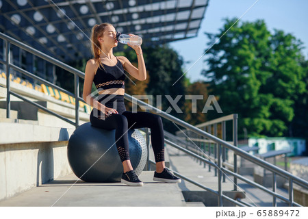 Water time. Woman leading healthy lifestyle drinking water before exercising on fitness ball 65889472