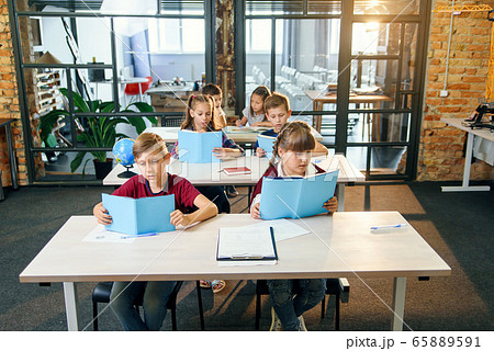 Group of six young happy pupils sit at their desk and reading educational books in the lesson. 65889591
