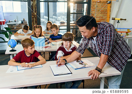 Pupils sit at desks and listens to the teacher while he explaining the topic of new lesson. 65889595