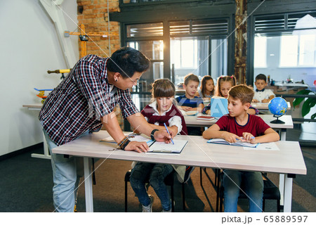 Pupils sit at desks and listens to the teacher while he explaining the topic of new lesson. 65889597