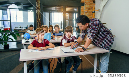 Teacher helping school kids with test tasks in classroom at primary school. 65889598