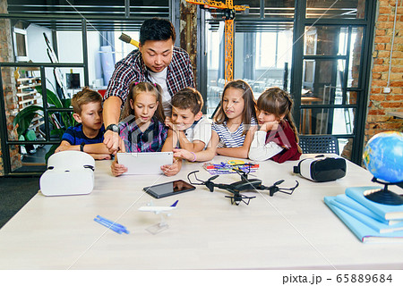 School teacher at desk works with five young pupils using digital tablet computer in technology class. Development, technology and modern education concept. 65889684