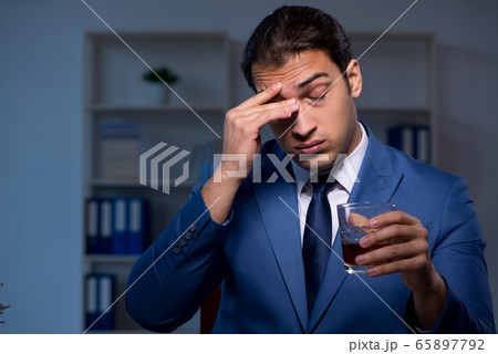 Alcohol addicted businessman working late in the office Alcohol addicted businessman working late in the office 65897792