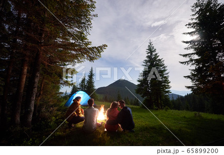 Loving couple surrounded by friends at an evening camping in the mountains. Loving couple surrounded by friends at an evening camping in the mountains. 65899200