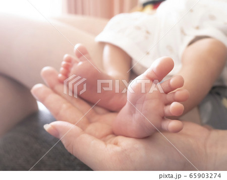 新生児の赤ちゃんが母の手のひらに足を乗せる愛らしいボディパーツの写真素材