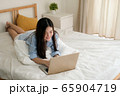 Cute asian woman wearing blue shirt lying down on bed using laptop for working at home. 65904719