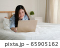 Cute asian woman wearing blue shirt lying down on bed using laptop for working at home. 65905162