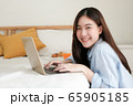 Young asian woman working on laptop computer while looking at the camera and smiling brightly in bedroom with breakfast,work from home concept. 65905185