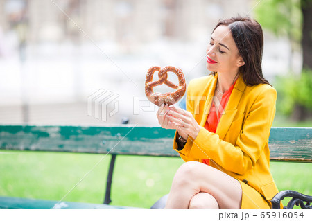 Beautiful young woman holding pretzel and relaxing in park 65916054