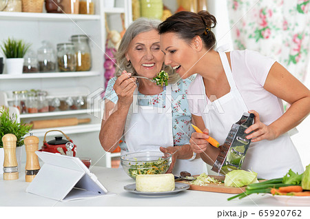 Smiling senior mother and adult daughter cooking together at kitchen Smiling senior mother and adult daughter cooking together at kitchen 65920762