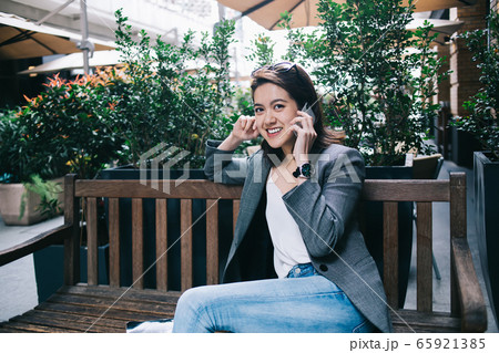 Smiling female talking on smartphone on bench 65921385