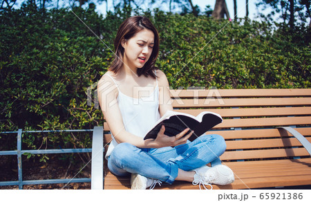Concentrating young woman reading book on bench 65921386