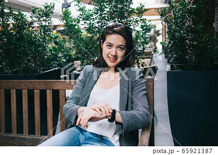 Smiling Asian woman checking watch on bench Smiling Asian woman checking watch on bench 65921387