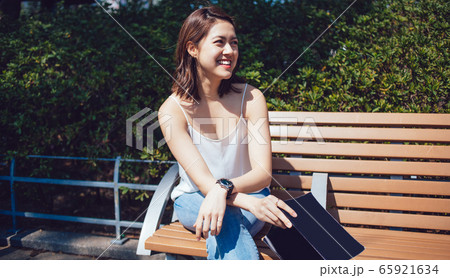 Young Asian smiling woman with book and arms crossed sitting on bench Young Asian smiling woman with book and arms crossed sitting on bench 65921634