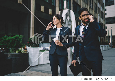 Multiracial colleagues speaking on smartphones in street Multiracial colleagues speaking on smartphones in street 65924217
