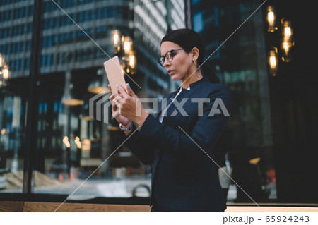 Smart female office worker in formal wear browsing digital tablet at city street 65924243